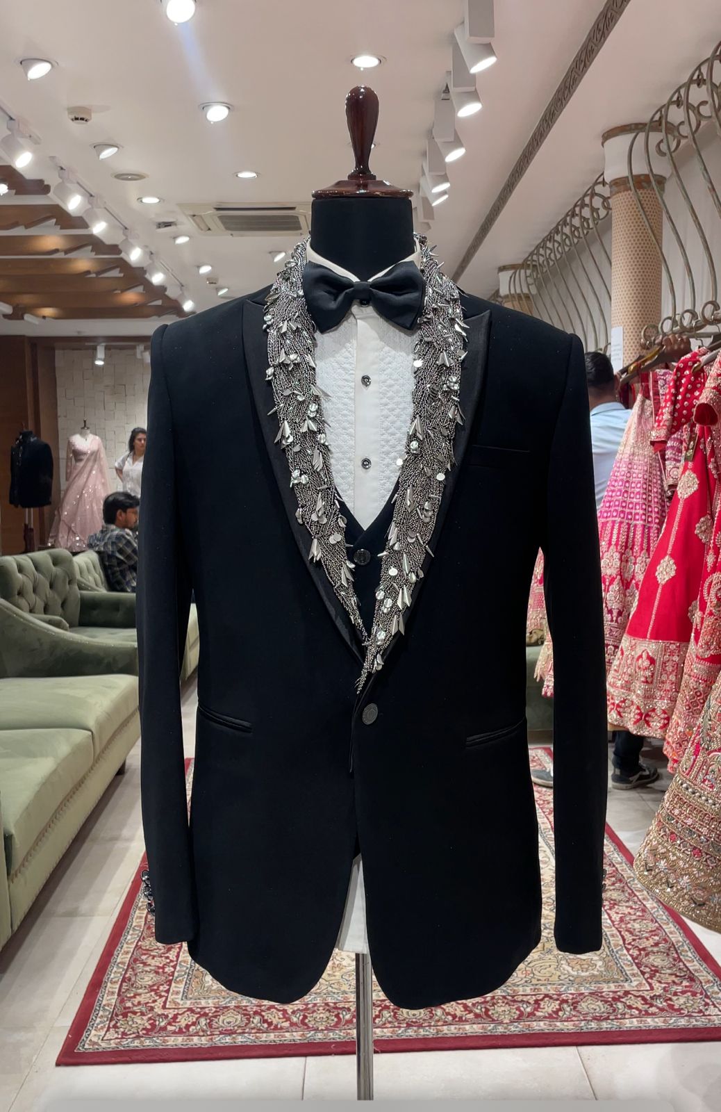 A black tuxedo with silver embellishments on a mannequin, featuring a jacket, waistcoat, bow tie, and a shirt with a decorative cuff.