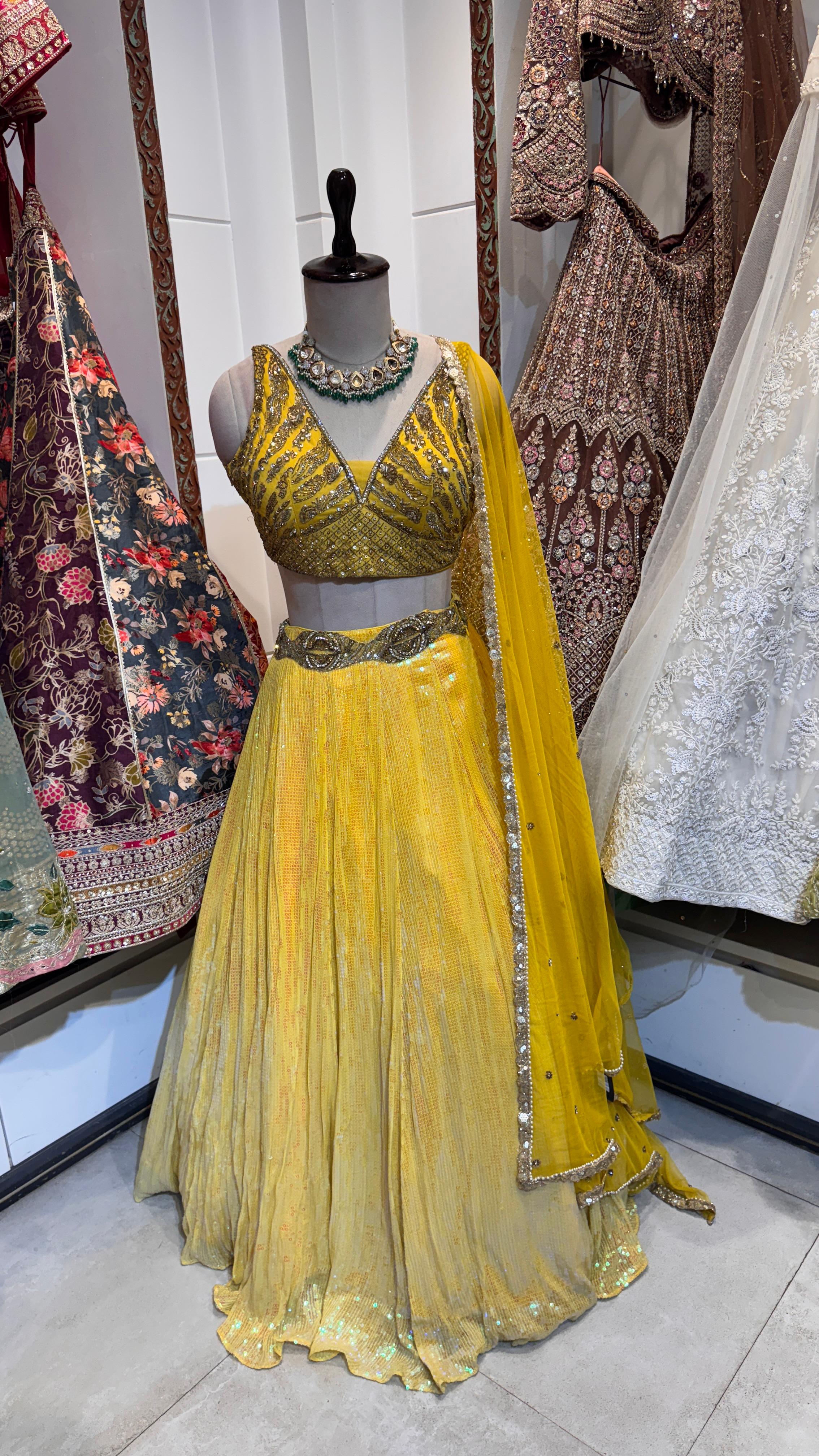 A yellow lehenga with sequins and embroidery, displayed on a mannequin, paired with a matching blouse and a dupatta with sequin-lined borders.