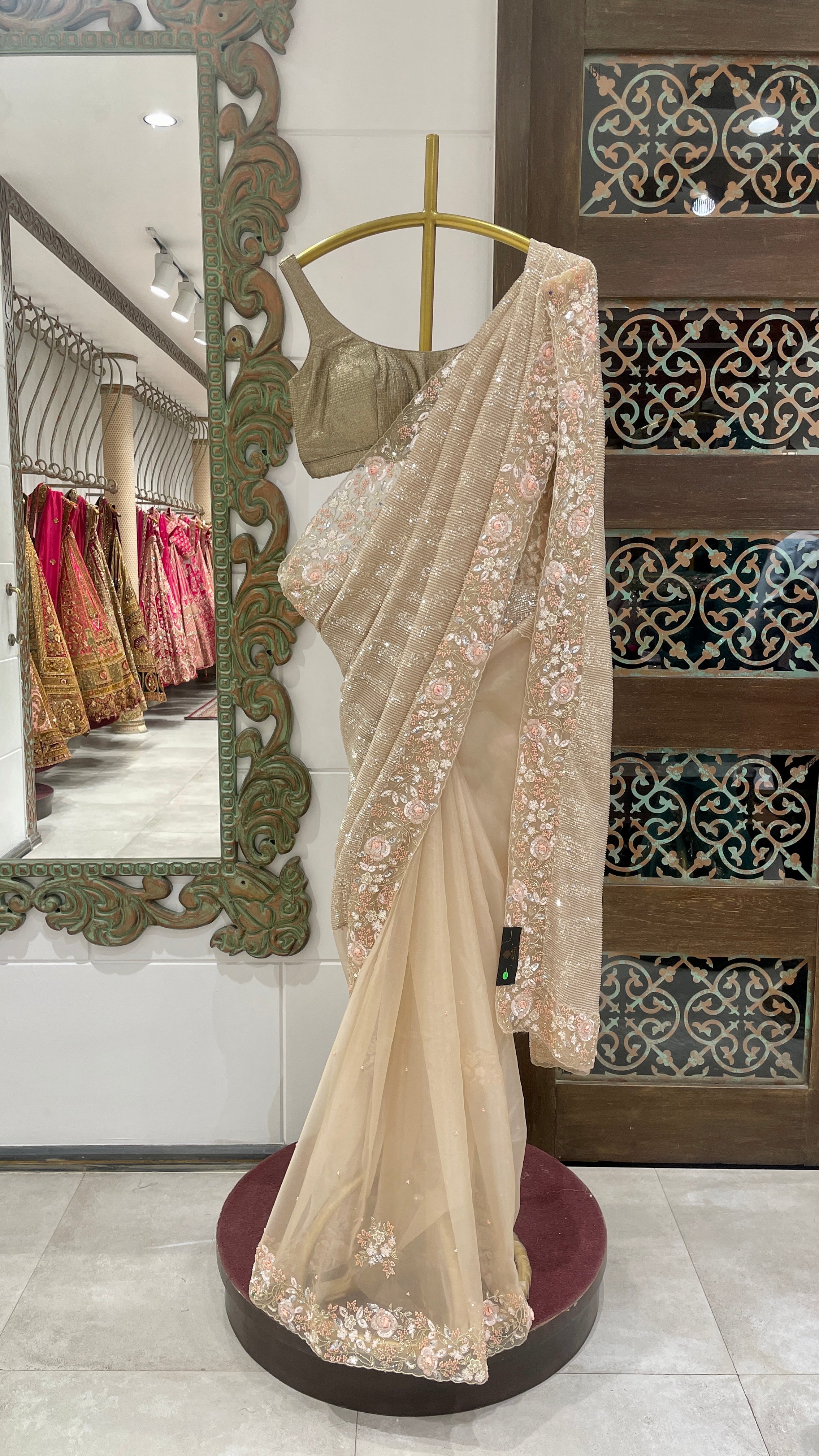 A gold sequins saree with floral embellishments displayed on a mannequin in a store with an unstiched blouse.