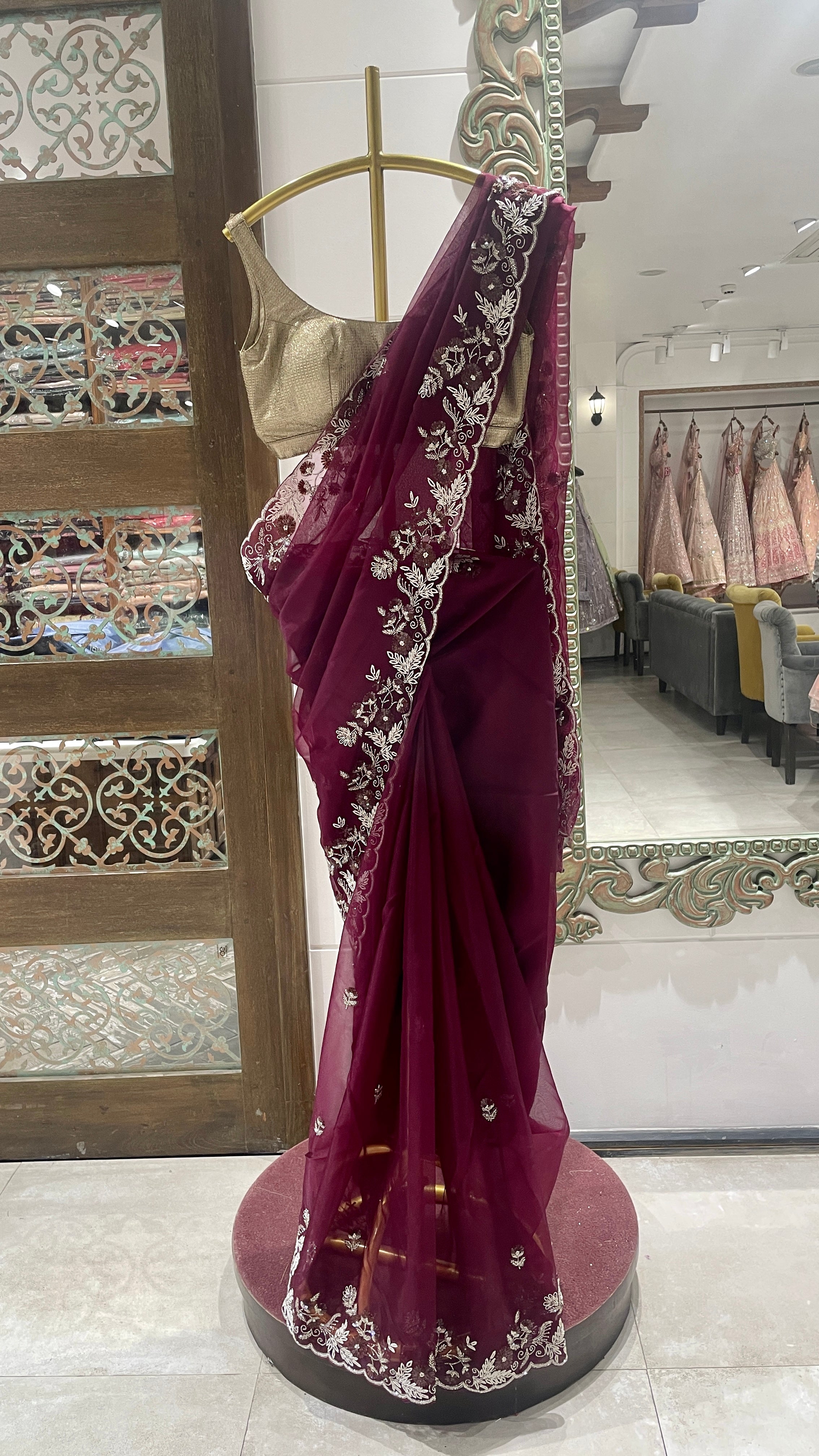 A violet organza saree with embellishments displayed on a mannequin in a store with intricate floral patterns and a golden border.
