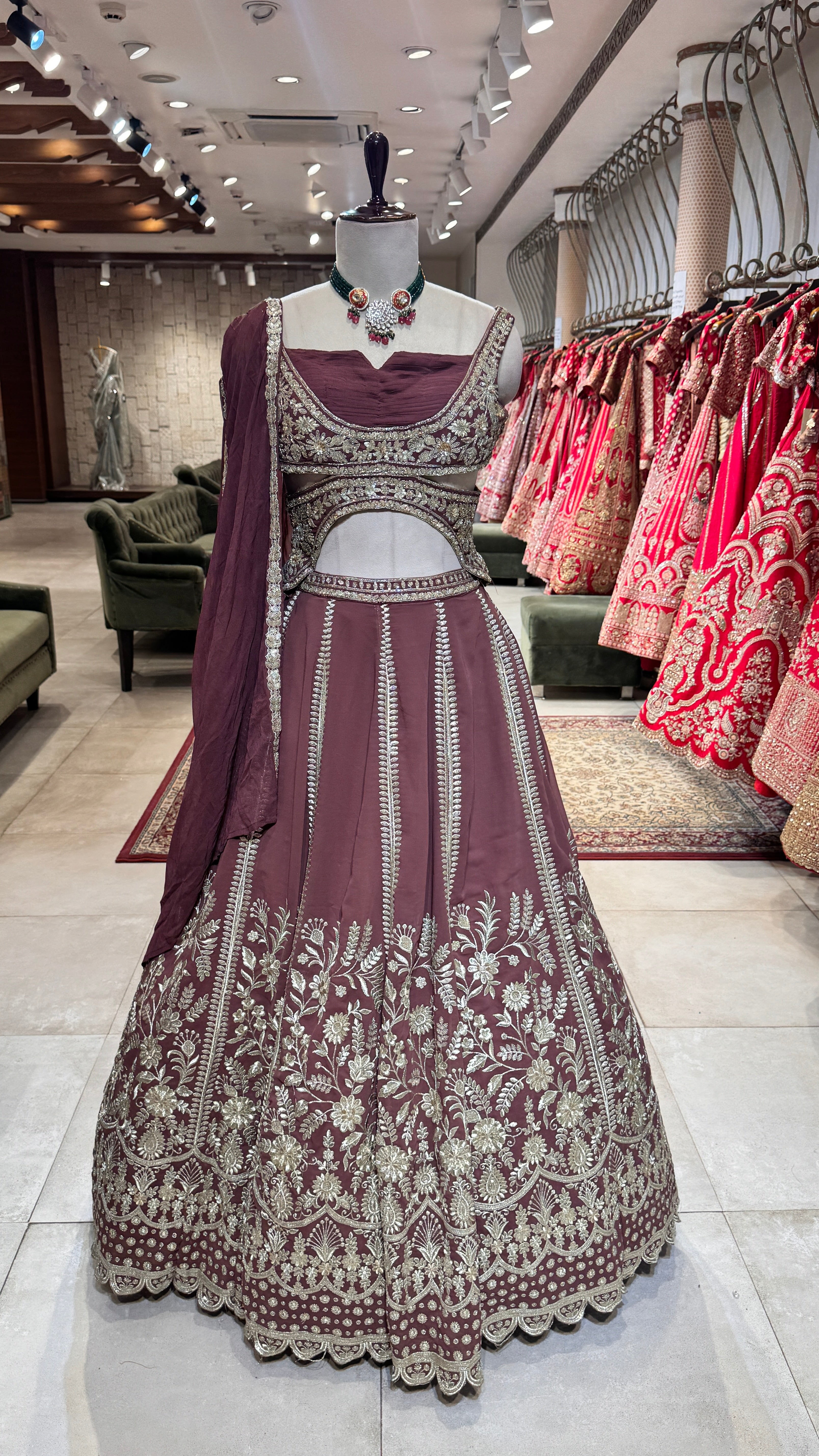 A deep maroon lehenga with intricate embroidery displayed on a mannequin, accompanied by a matching blouse and dupatta with embroidered borders.