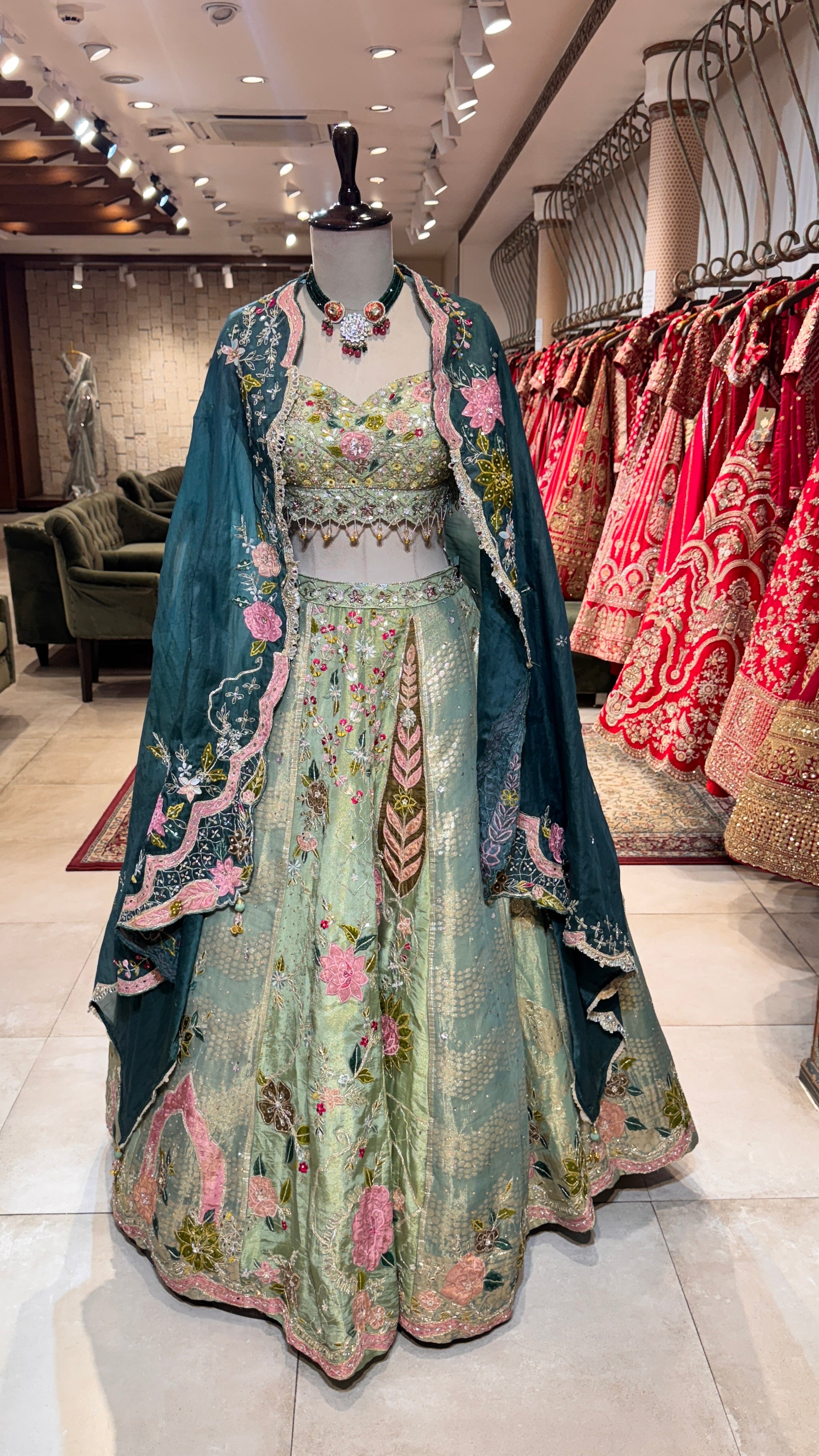 A mannequin displaying a green lehenga with embroidery and a matching blouse, paired with a sheer dupatta, indicating a traditional or festive outfit.