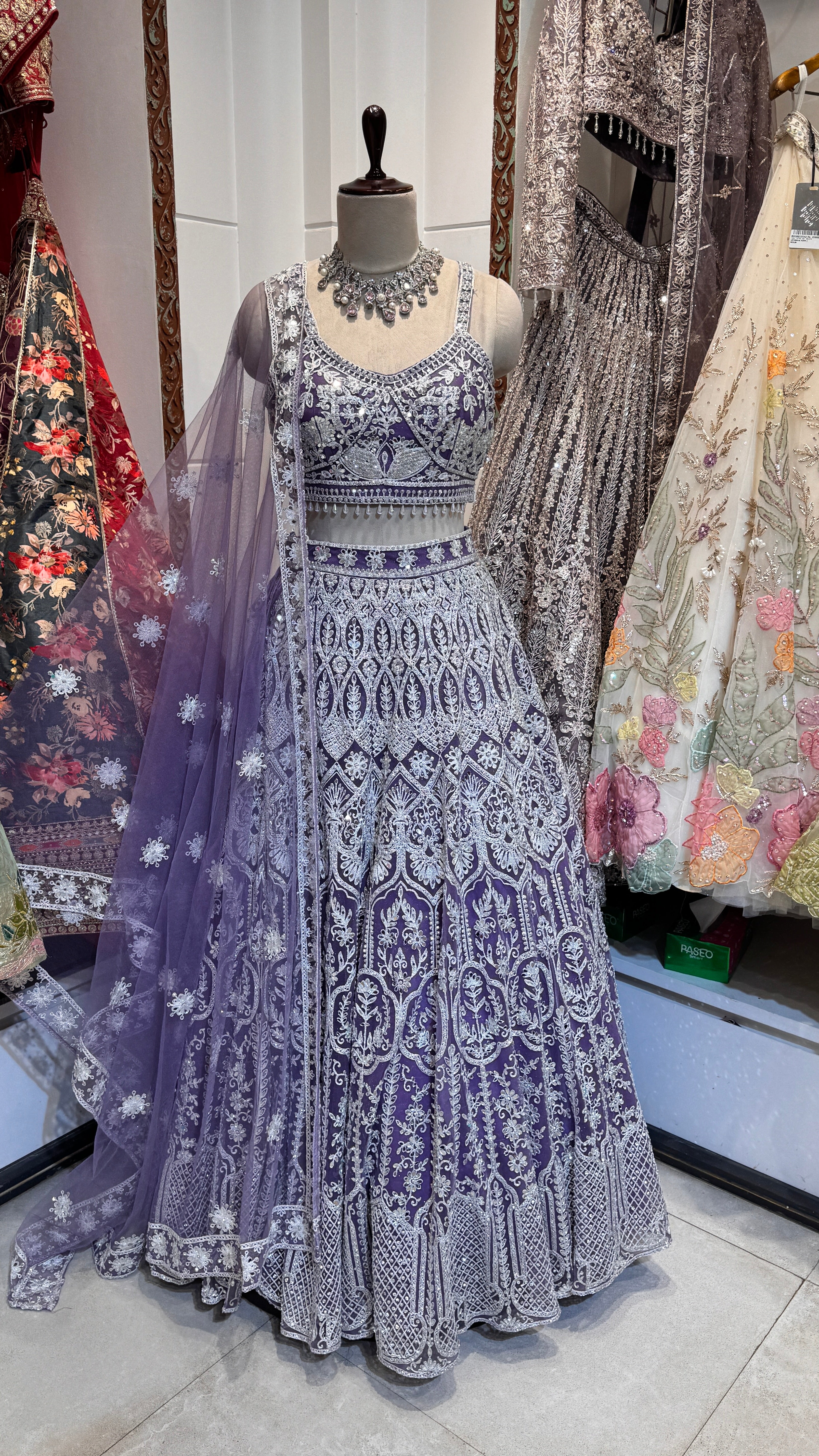 A mannequin displaying a purple lehenga with silver embroidery, paired with a matching blouse and a sheer dupatta with silver borders.