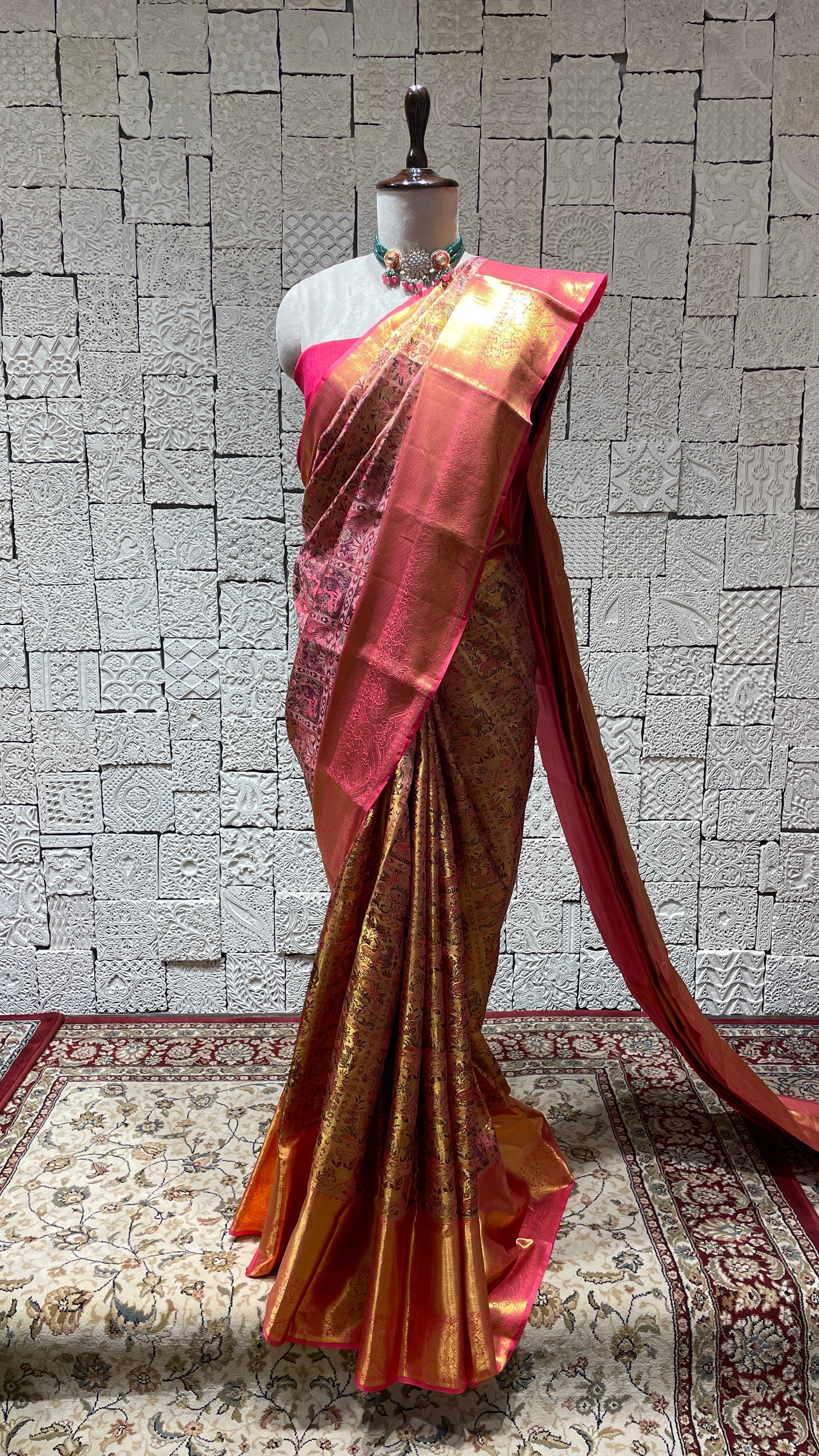 A draped pink Kanjivaram silk saree on a mannequin, featuring intricate golden embroidery and a flowing design.