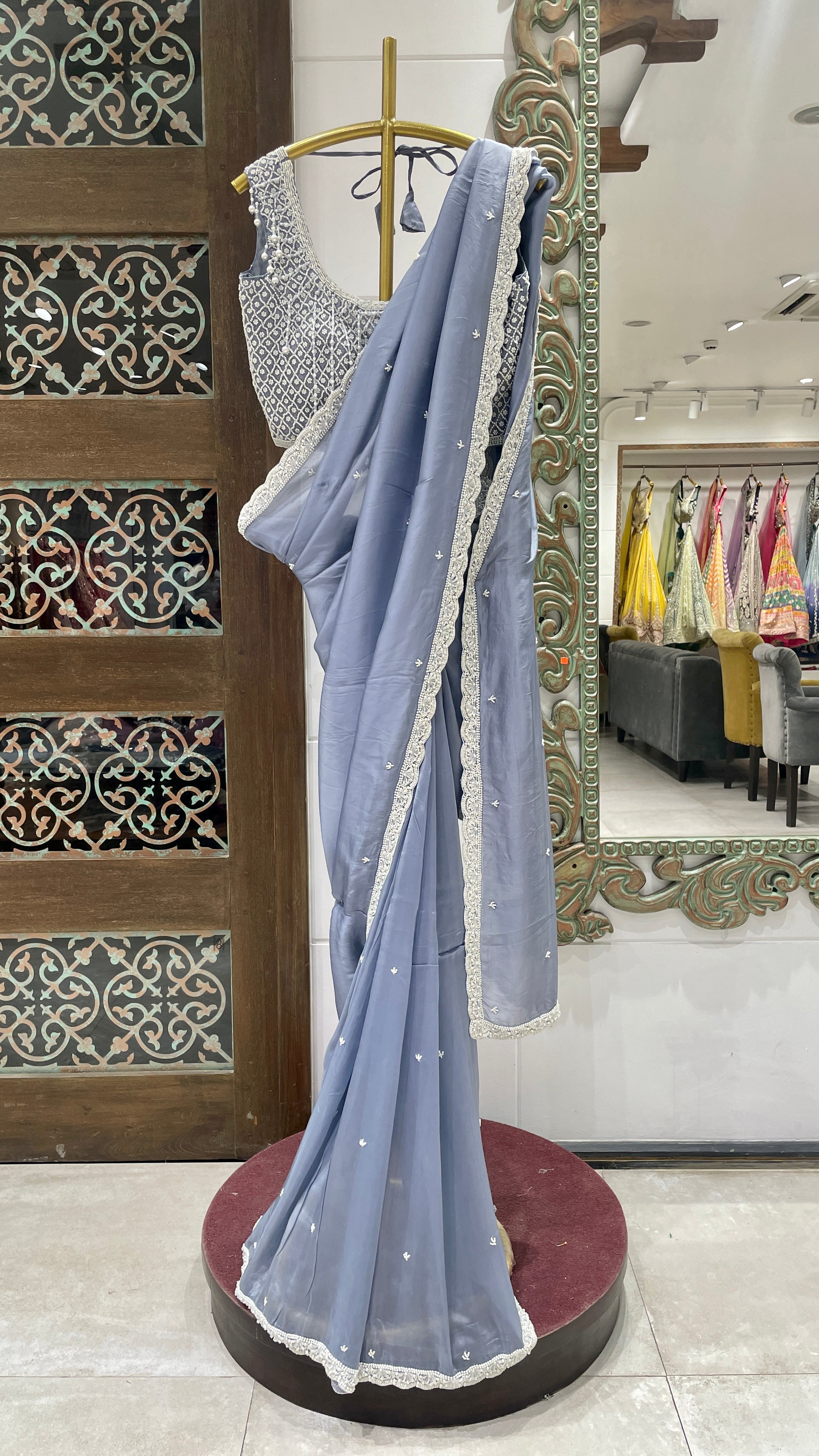 A lilac crape saree with pearl embellishments displayed on a mannequin in a store with various other sarees in the background.