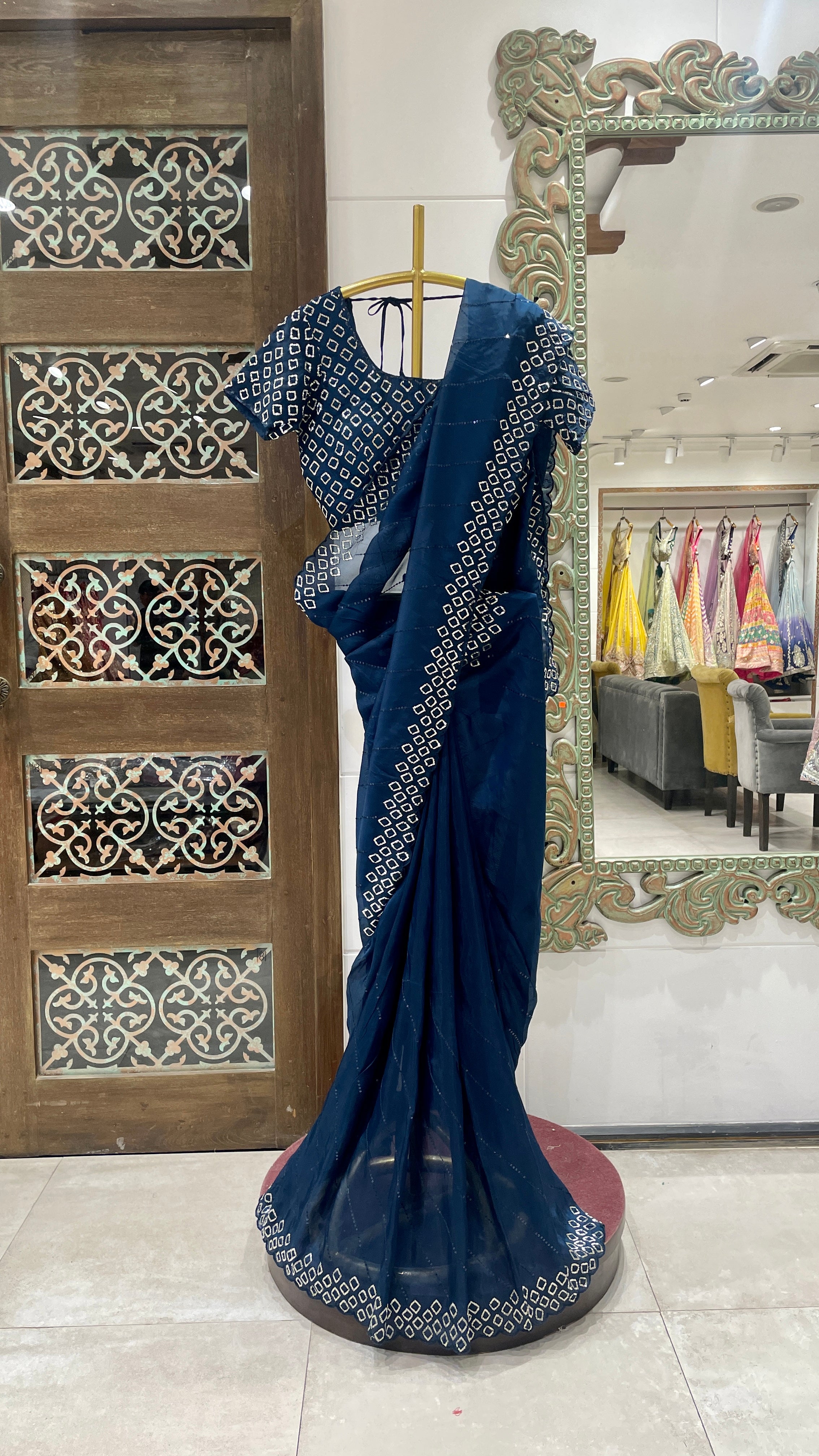 A blue organza saree with cutdana embellishments displayed on a mannequin in a store with intricate patterns on the walls in the background.