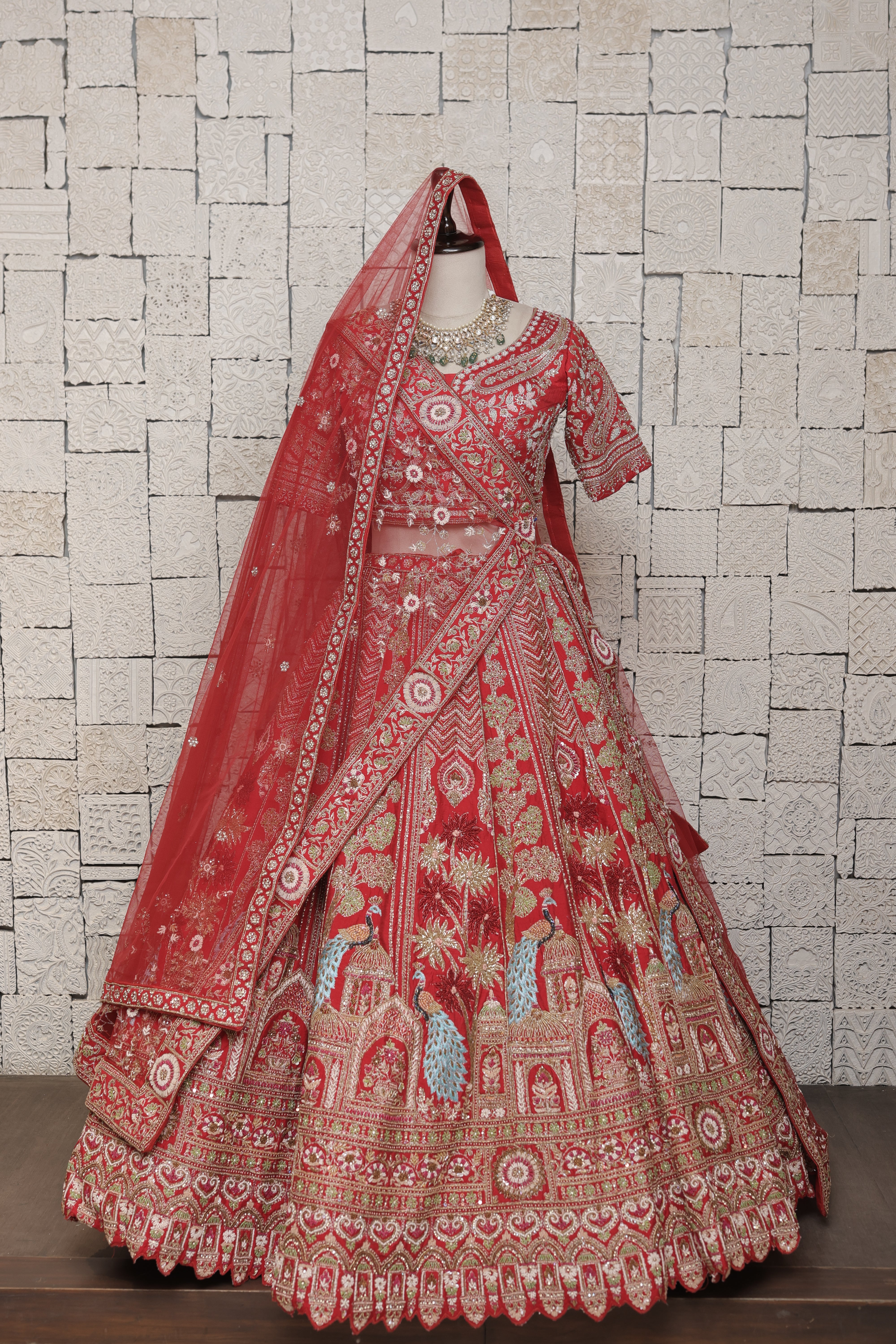 A mannequin displaying a red bridal lehenga with peacock motifs and heavy zari embroidery, accompanied by a dupatta with a border.