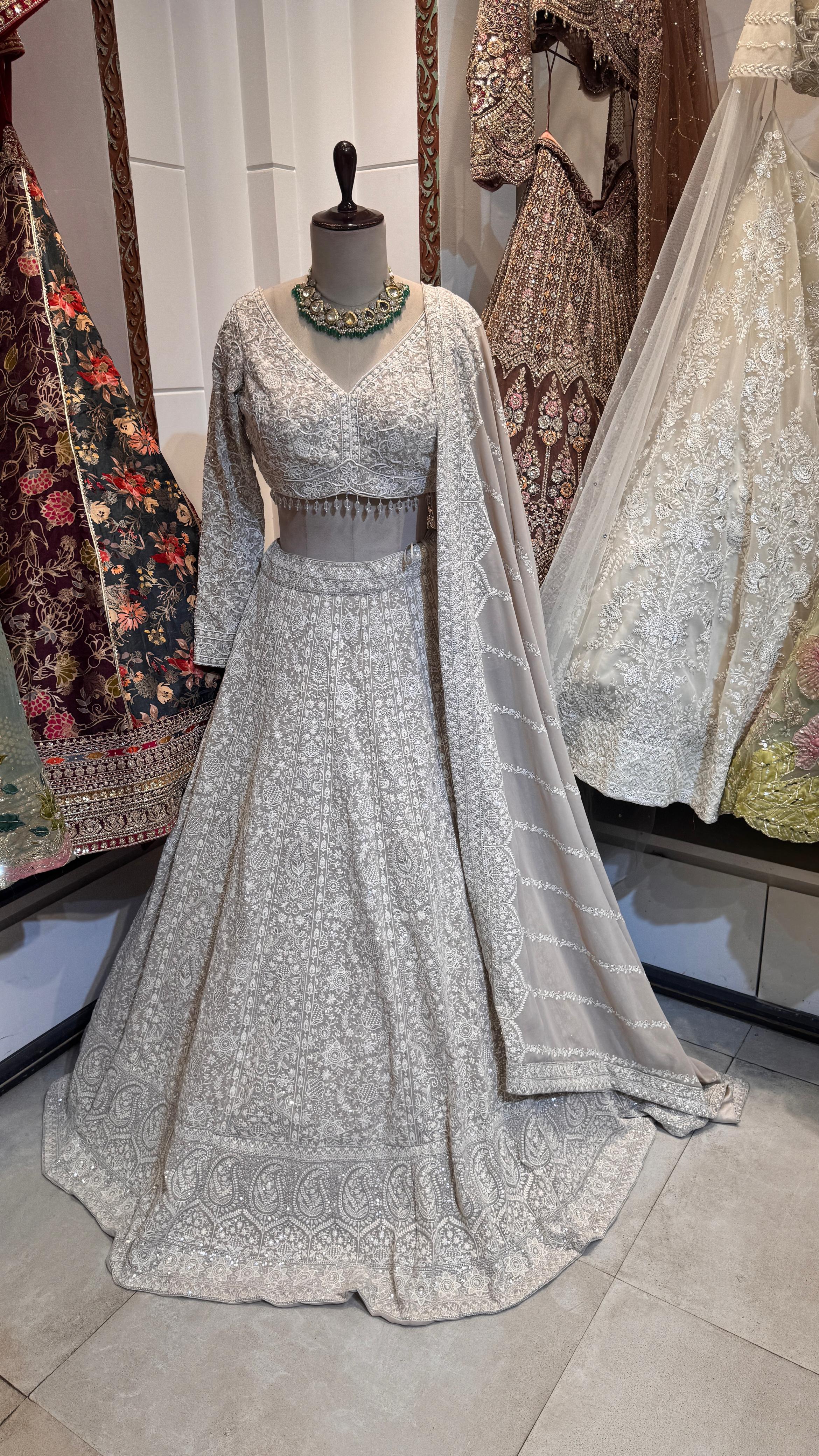 A mannequin displaying a white lehenga with pearl work and a matching blouse, paired with a sheer dupatta with pearl-studded borders.