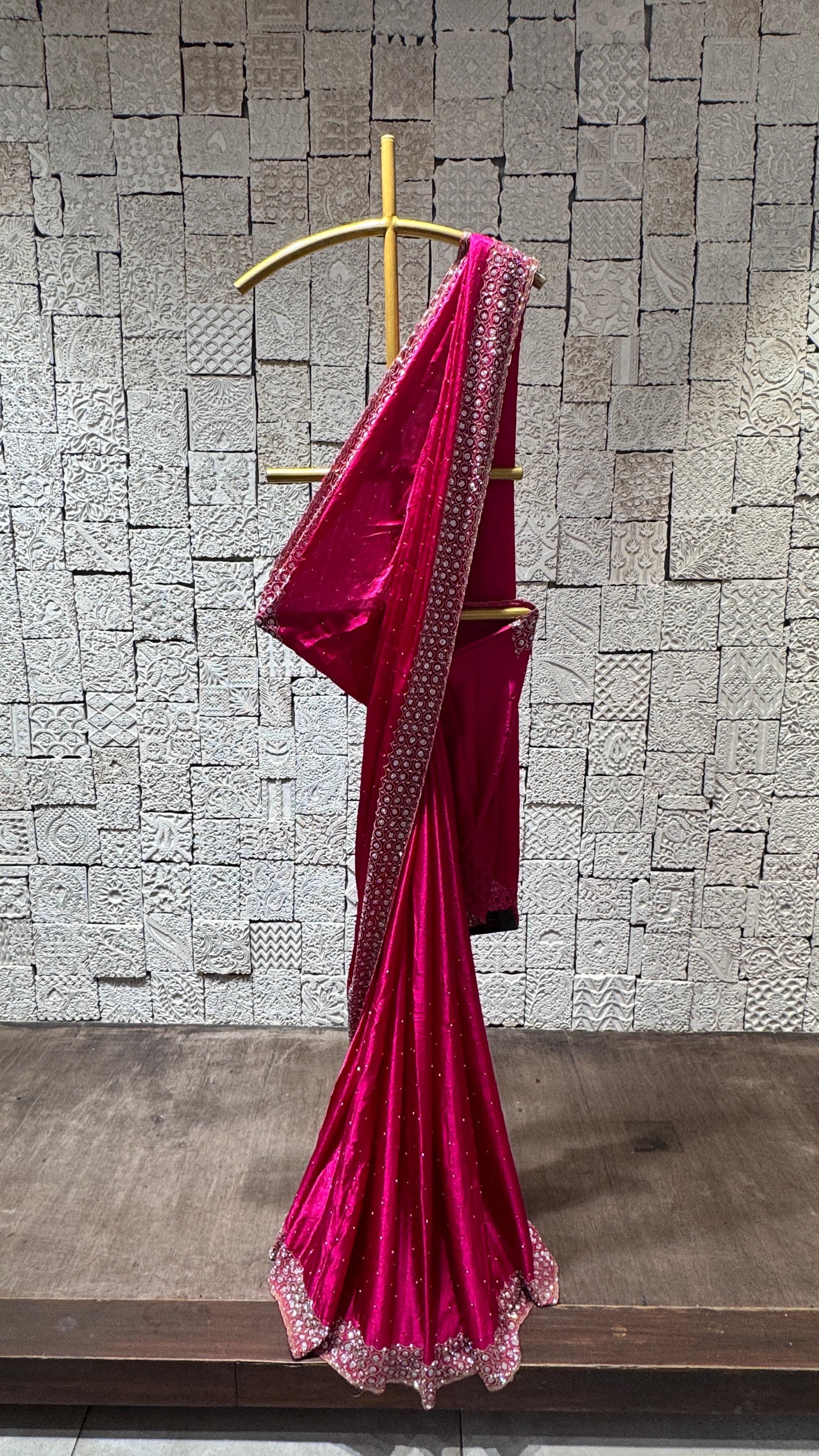 A hot pink saree with pebbles embroidery displayed on a hanger against a brick wall background.