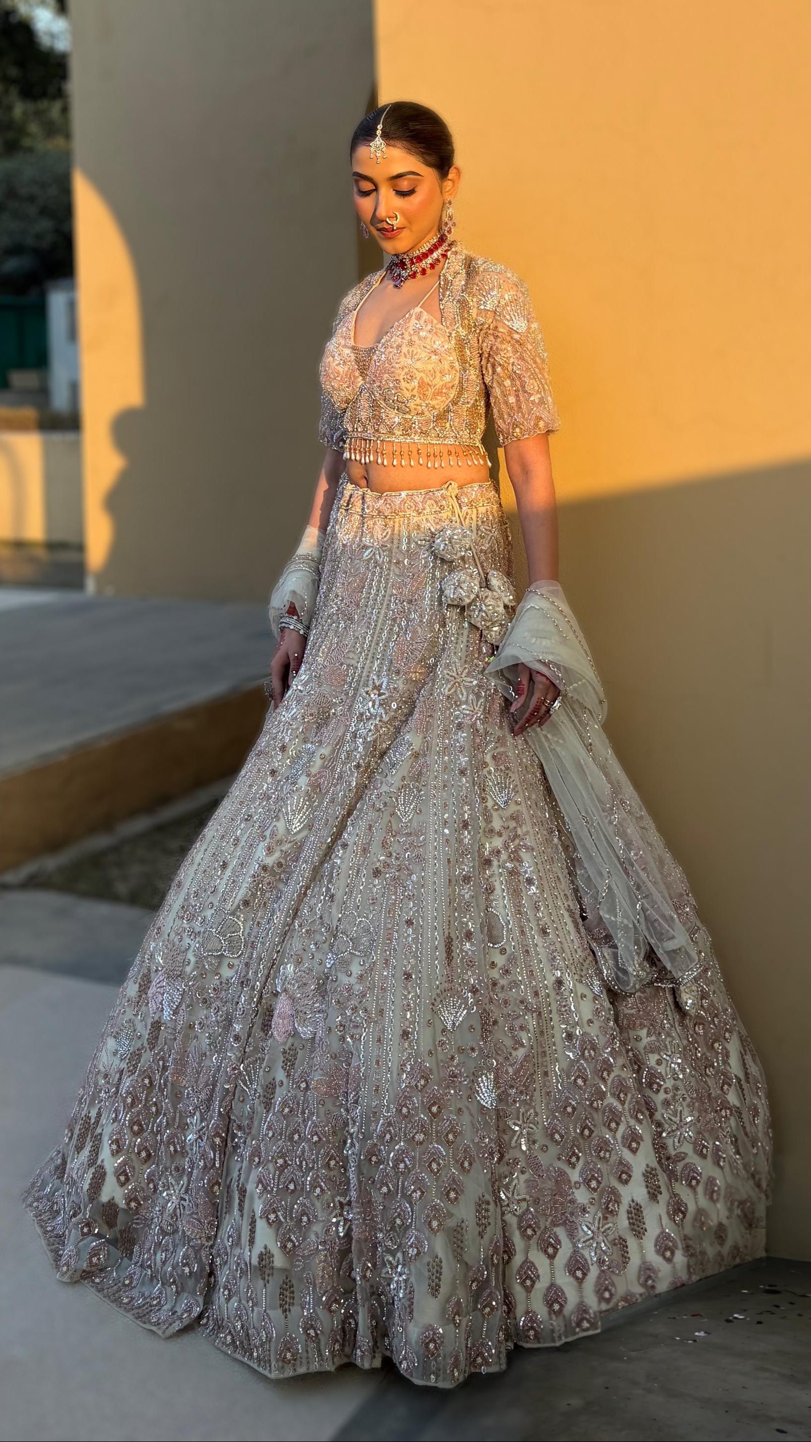 Woman in a traditional embroidered outfit standing against a warm-toned wall.